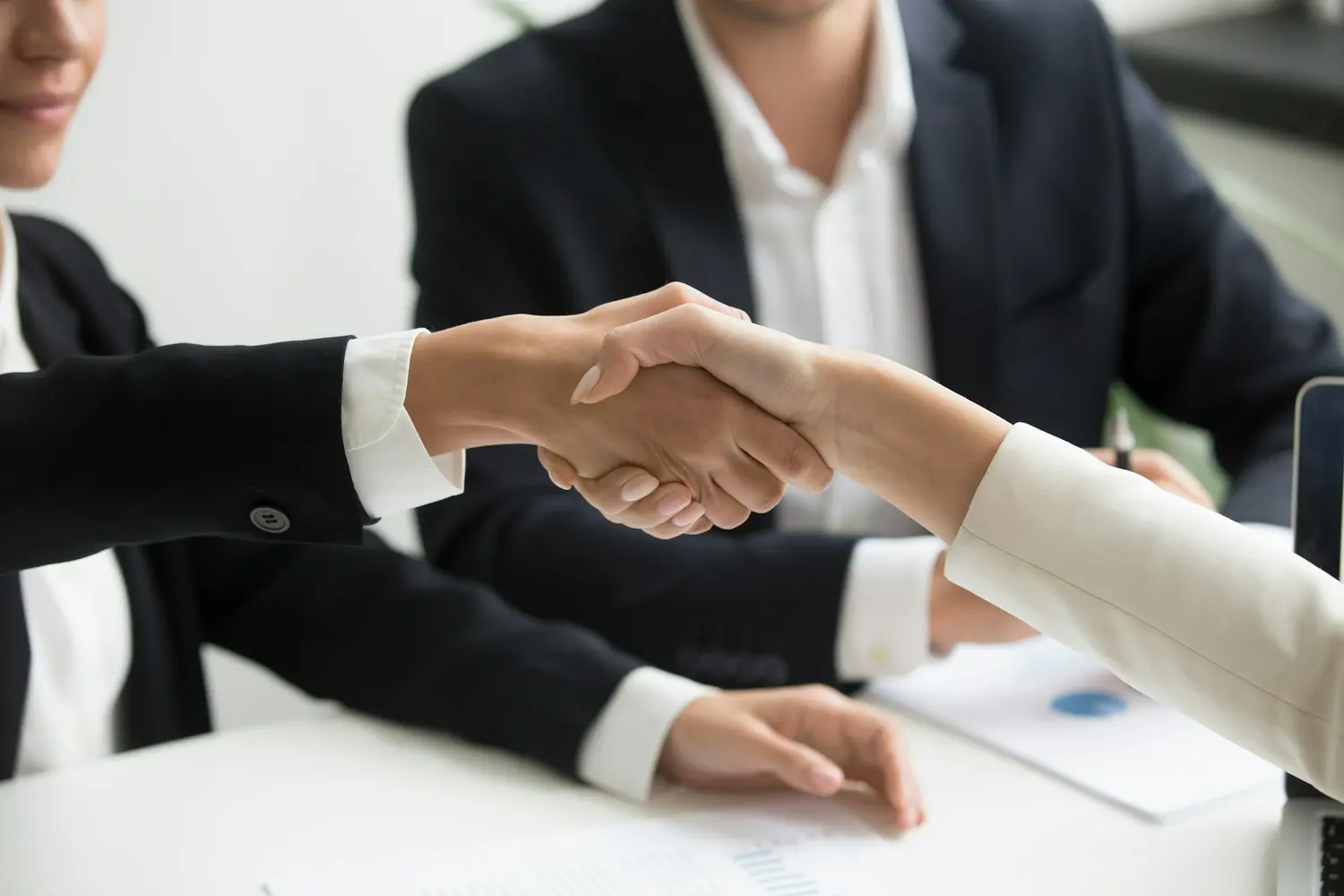 A handshake across a meeting table as two parties agree terms